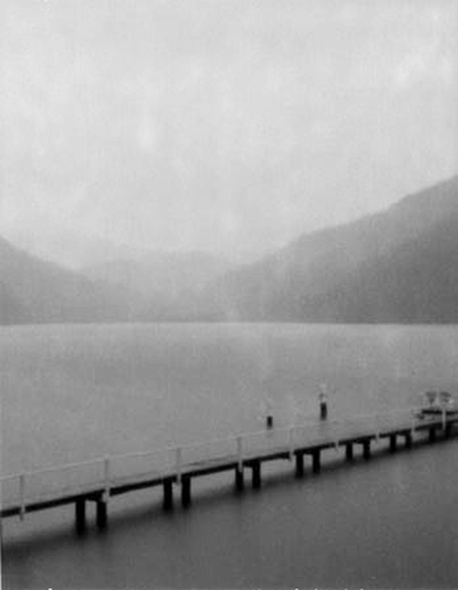 Black-and-white photograph of a jetty and distant hills across Woy Woy Bay in rain.
