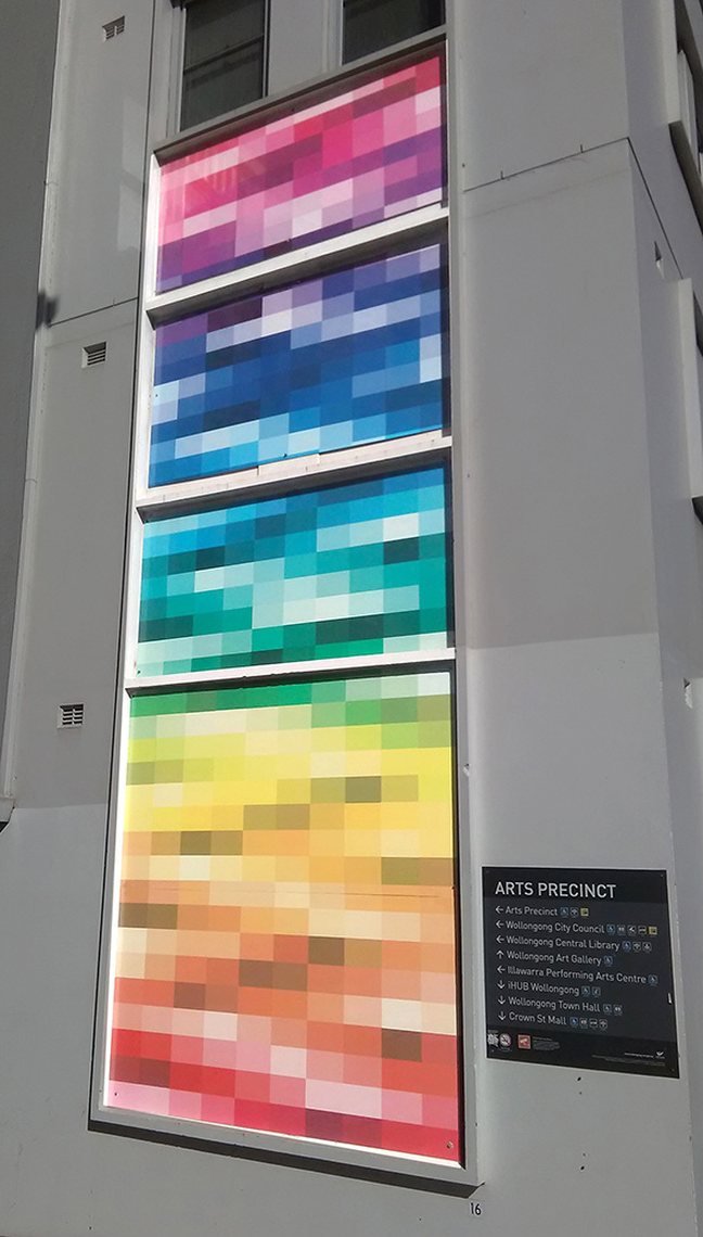 A tall vertical mural of pixelated colour fields, from magenta through blue and green to yellow, on the north wall of Wollongong City Gallery.